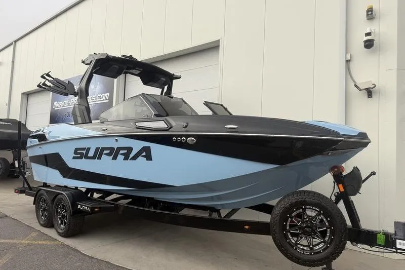 Slide: The Image of 2025 Supra SL 575 boat in blue and black on a trailer outside a building. - 5
