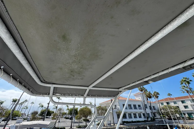 Slide: The Image of 1993 Blackfin Sportfisher boat canopy with visible wear, docked near palm trees and buildings. - 28