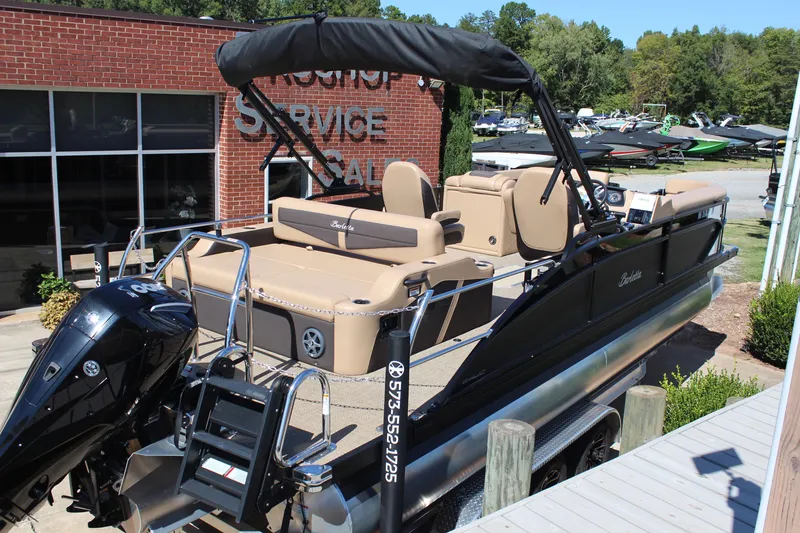 Slide: The Image of 2025 Barletta C24UC pontoon boat with tan seating and black canopy at dealership. - 4