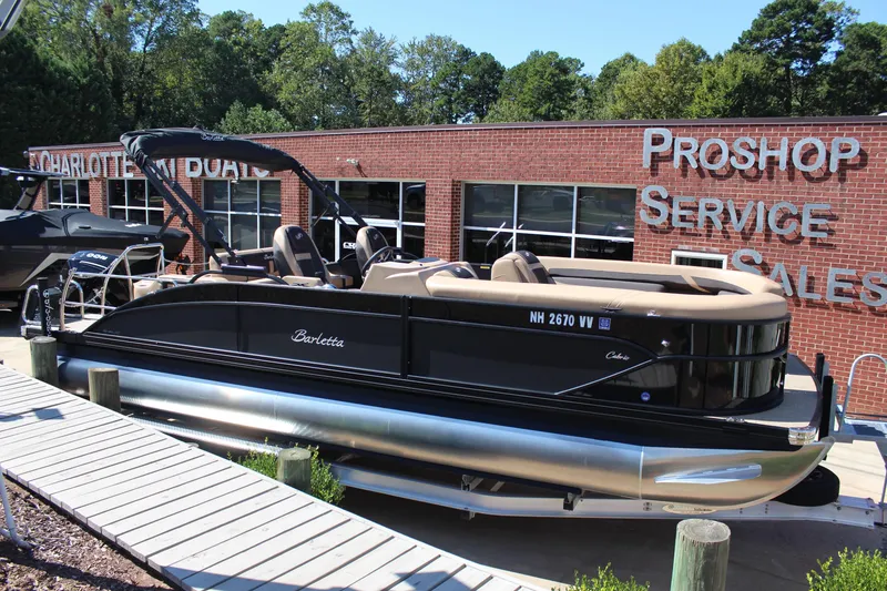 Slide: The Image of 2025 Barletta C24UC pontoon boat displayed at dealership, sunny day. - 5