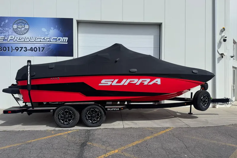 Slide: The Image of 2025 Supra SL 575 boat with cover on trailer, parked outside a building. - 16
