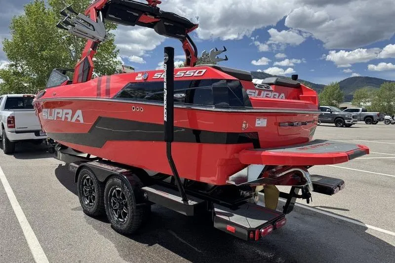Slide: The Image of 2025 Supra SL 575 boat in vibrant red, parked on a trailer under a partly cloudy sky. - 3