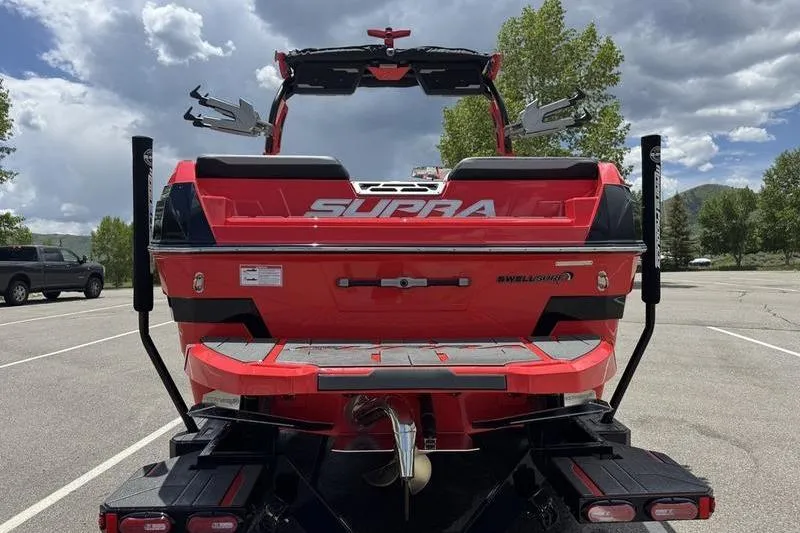 Slide: The Image of 2025 Supra SL 575 boat, red exterior, parked outdoors under cloudy sky. - 4