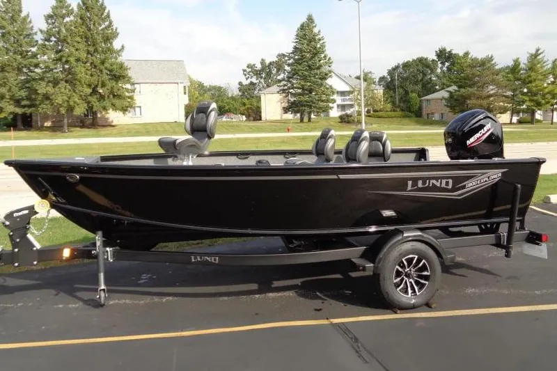 The Image of 2026 Lund 1800 Explorer Tiller boat on trailer, parked outdoors with trees in background. - 0