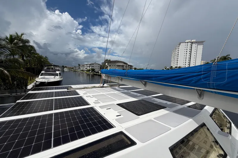 Slide: The Image of 2023 Royal Cape Catamarans Majestic 530 with solar panels, docked by a scenic waterfront. - 23