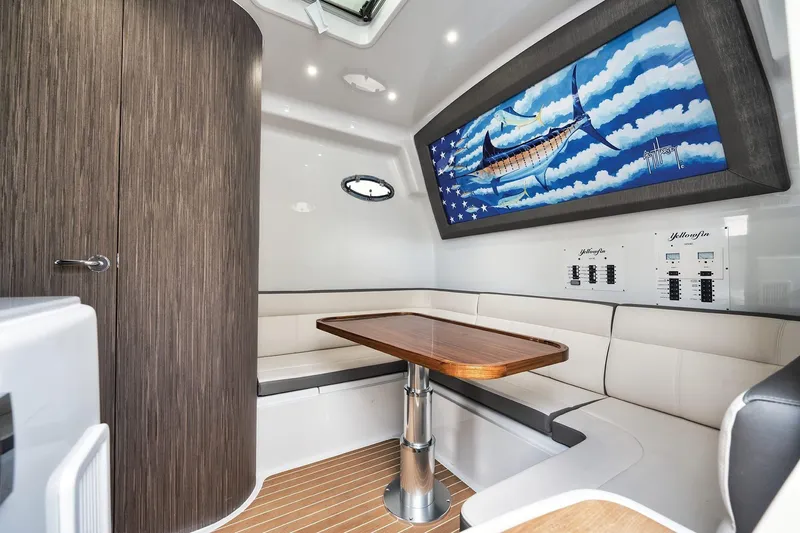 Slide: The Image of 2022 Yellowfin 54 Offshore cabin with seating, wooden table, and marlin artwork. - 15