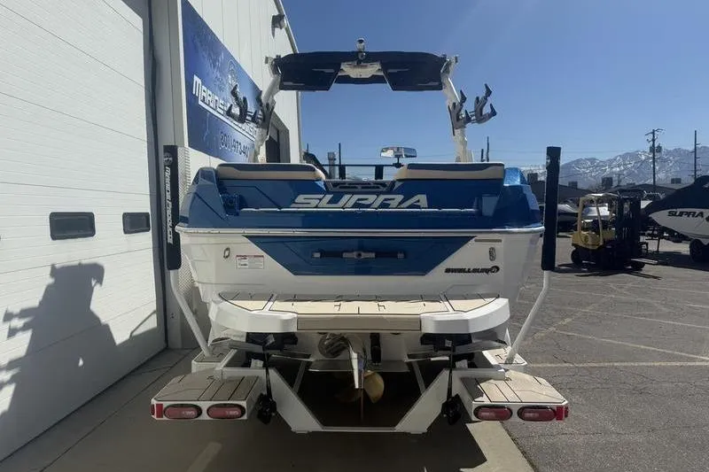Slide: The Image of 2025 Supra SV 575 boat, blue and white, parked outside dealership with mountain backdrop. - 2