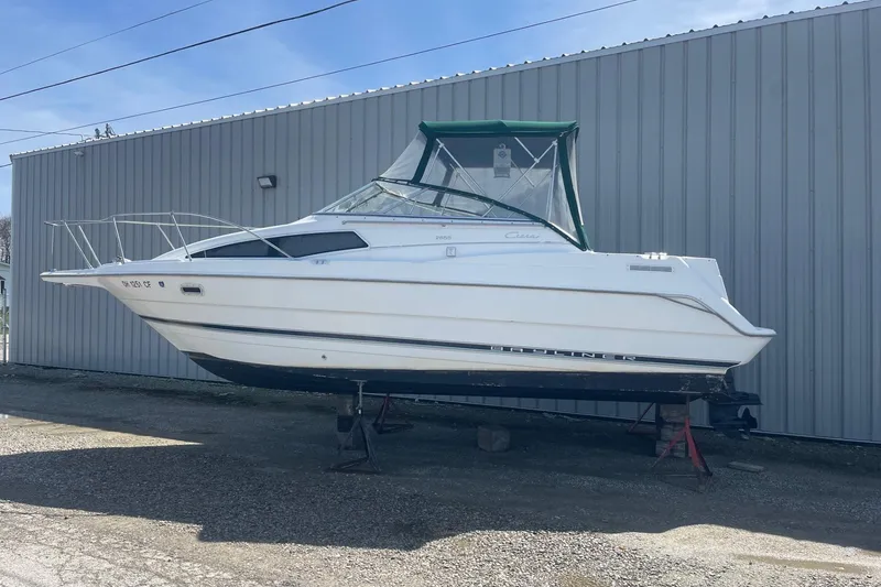 Slide: The Image of 1997 Bayliner 2655 Ciera boat on stands, white hull, green canopy, parked by metal building. - 12