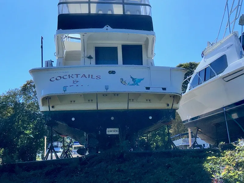 Slide: The Image of 2004 Silverton 38 Convertible boat named "Cocktails" on land, surrounded by trees and other boats. - 18