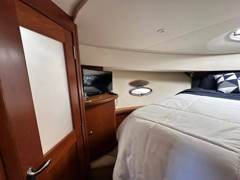 Slide: The Image of 2004 Silverton 38 Convertible yacht bedroom with TV, wooden cabinetry, and cozy bedding. - 49