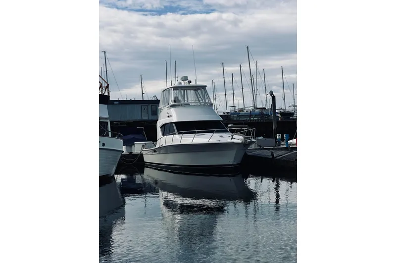 Slide: The Image of 2000 Riviera 40 yacht docked at marina, reflecting on calm water under cloudy sky. - 94