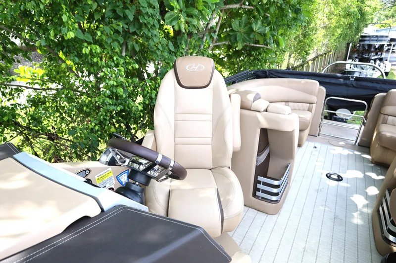 Slide: The Image of 2019 Harris Grand Mariner 250 interior with beige seating and steering wheel, surrounded by greenery. - 14