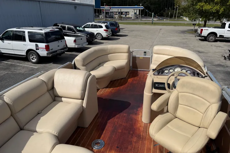 Slide: The Image of 2013 Berkshire 24RFC pontoon boat with beige seating and wooden deck, parked outdoors. - 9