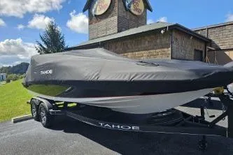 Slide: The Image of 2024 Tahoe 2150 boat covered, parked outdoors near a rustic building. - 13