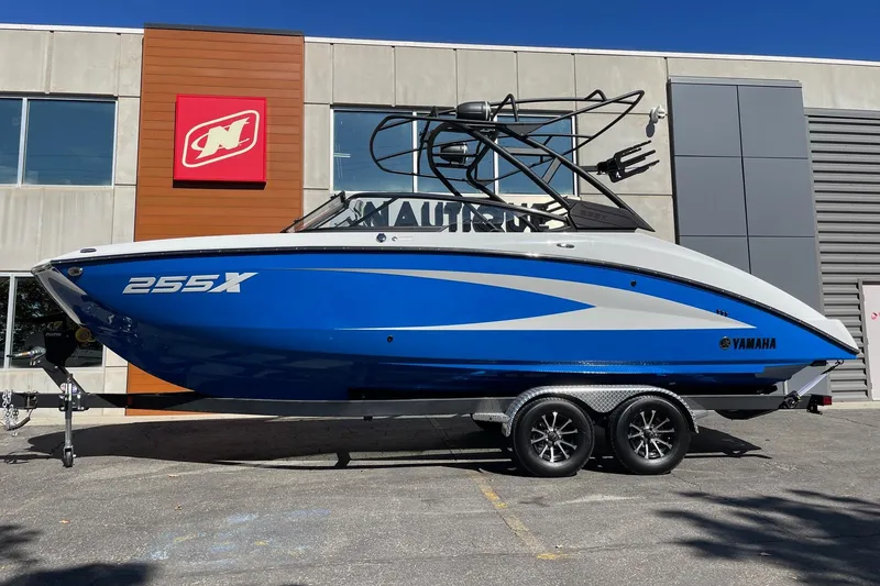 The Image of 2025 Yamaha Boats 255XD in blue, parked on a trailer outside a building. - 1