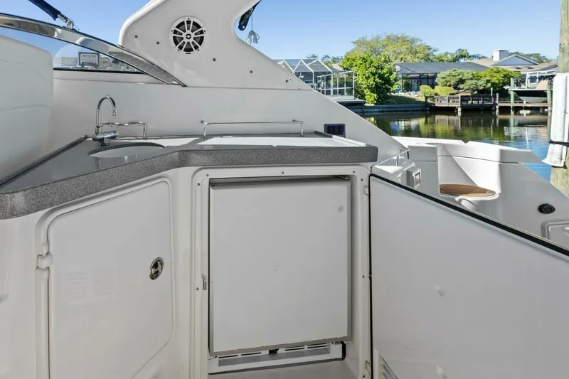 Slide: The Image of 2005 Regal Commodore 3560 yacht kitchenette with sink and storage, docked by waterfront homes. - 18
