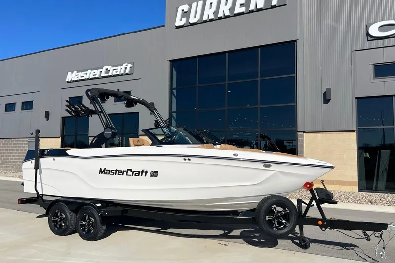 The Image of 2025 MasterCraft XT23 boat on trailer outside dealership building. - 1