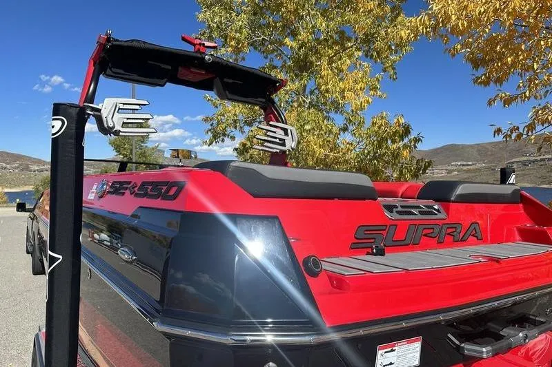 Slide: The Image of 2024 Supra SE 575 boat, red and black, parked near a lake with autumn trees. - 2