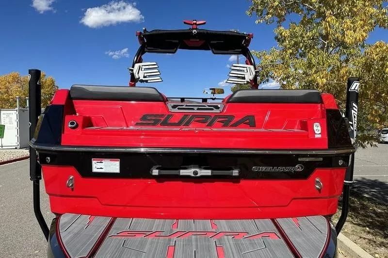 Slide: The Image of 2024 Supra SE 575 boat, red exterior, rear view, parked outdoors under blue sky. - 3