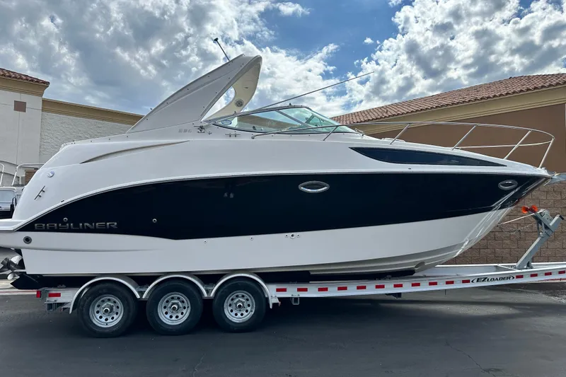 Slide: The Image of 2012 Bayliner 285 Cruiser on trailer, parked outdoors under cloudy sky. - 2