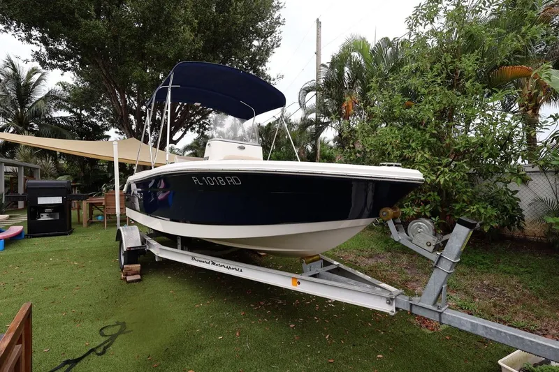 The Image of 2016 Robalo R160 Center Console boat on trailer, surrounded by lush greenery. - 0