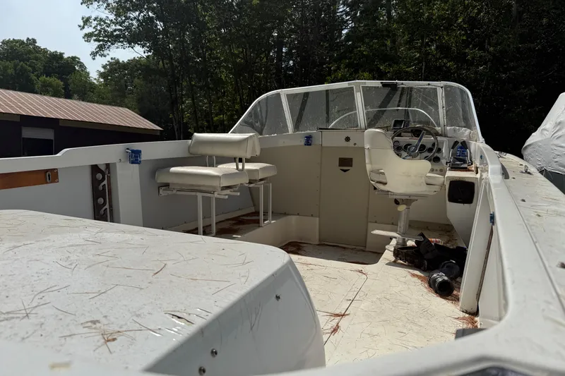 Slide: The Image of 1965 Bertram boat interior with steering wheel and seating, surrounded by trees. - 24