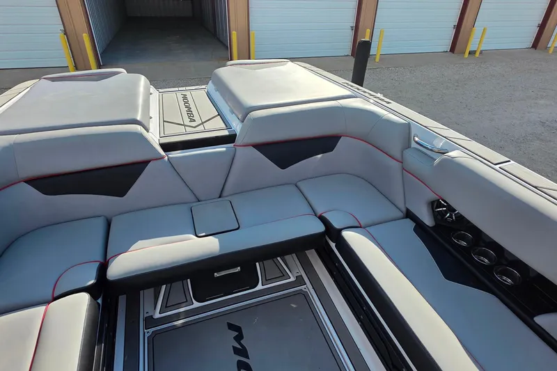 Slide: The Image of 2020 Moomba Makai boat interior with gray seating and red accents, docked near storage units. - 14
