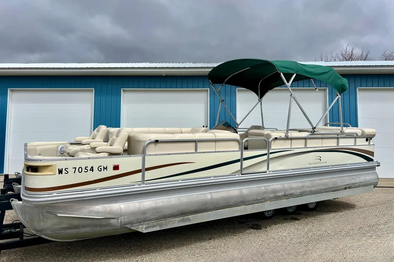 The Image of 2006 Bennington 2575 FS pontoon boat with green canopy, parked near blue garage doors. - 0