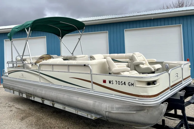 Slide: The Image of 2006 Bennington 2575 FS pontoon boat with green canopy, parked near blue building. - 2