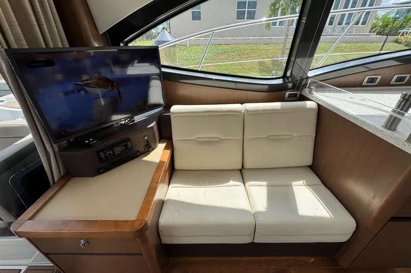 Slide: The Image of Interior of 2016 Sea Ray 400 Sundancer with TV, beige seating, and wood accents. - 13