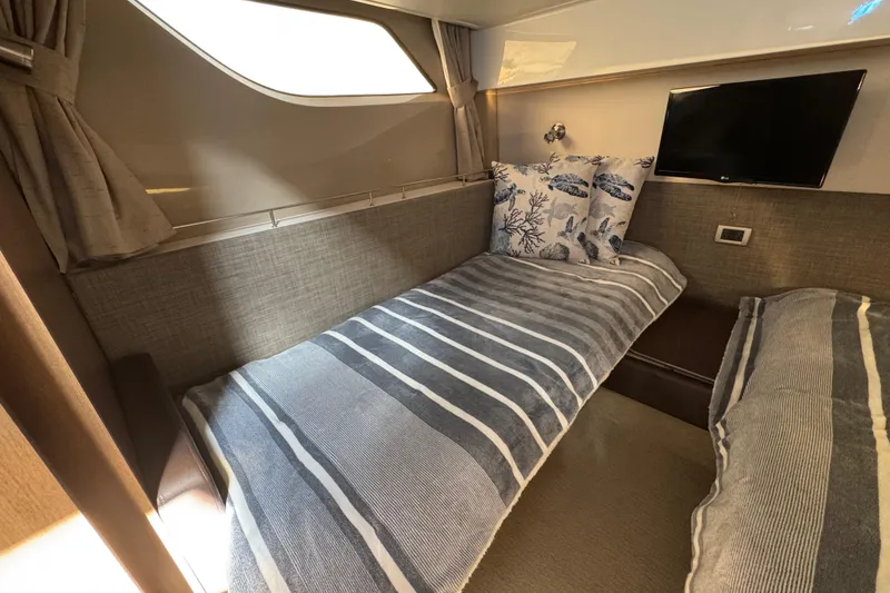 Slide: The Image of 2016 Sea Ray 400 Sundancer cabin with twin beds, striped bedding, and a wall-mounted TV. - 37