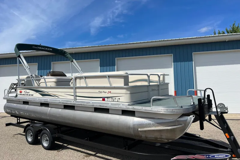 The Image of 2006 Sun Tracker Party Barge 24 pontoon boat on trailer, parked near blue building. - 1