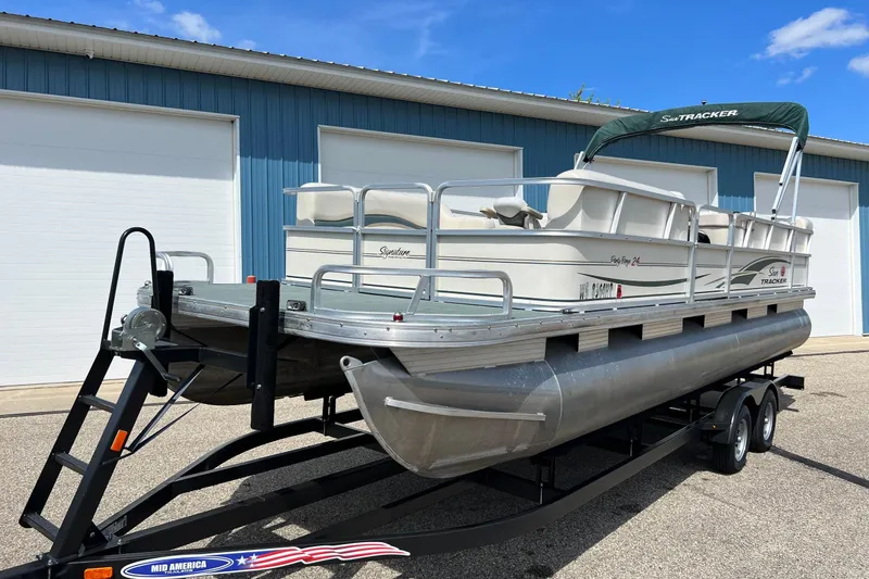 Slide: The Image of 2006 Sun Tracker Party Barge 24 pontoon boat on trailer, parked outside blue building. - 4