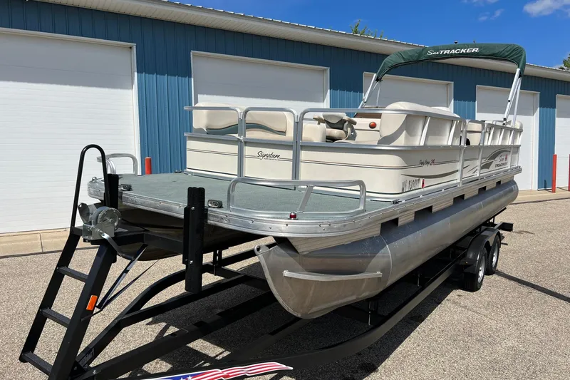 Slide: The Image of 2006 Sun Tracker Party Barge 24 pontoon boat on trailer, parked near blue building. - 5