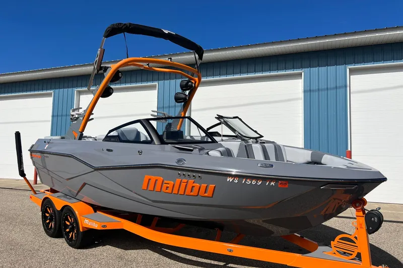 Slide: The Image of 2023 Malibu Wakesetter 22 LSV boat on orange trailer, parked outside blue building. - 2