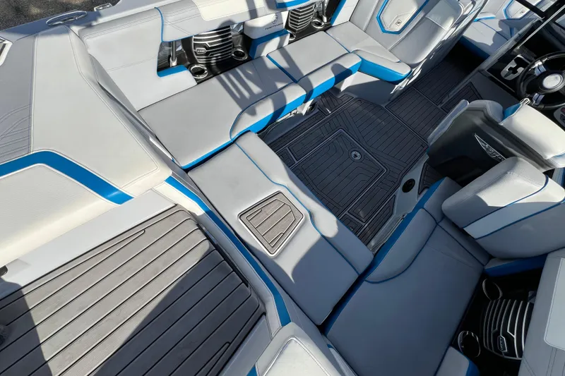 Slide: The Image of 2020 Super Air Nautique G21 interior with gray and blue seating, cup holders, and textured flooring. - 16