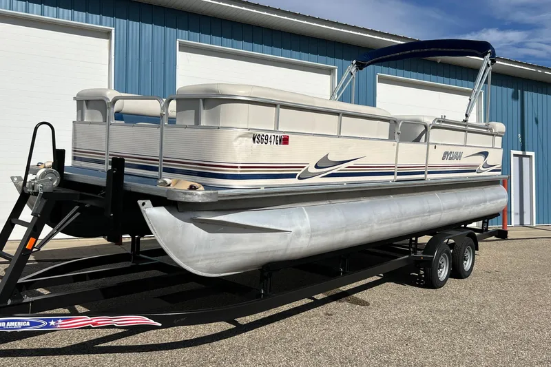 Slide: The Image of 2003 Sylvan 824 Mirage Cruise pontoon boat on trailer, parked near blue building. - 19