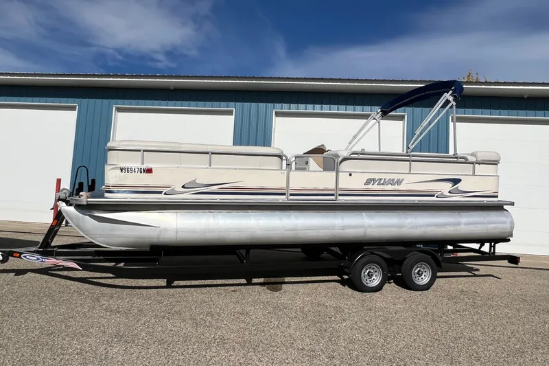 Slide: The Image of 2003 Sylvan 824 Mirage Cruise pontoon boat on trailer, parked outside blue building. - 21