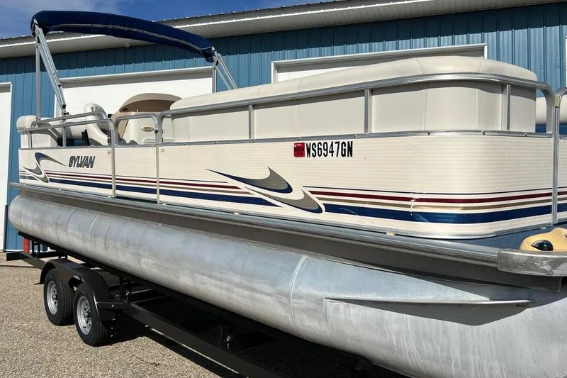 Slide: The Image of 2003 Sylvan 824 Mirage Cruise pontoon boat on trailer, parked near blue building. - 5