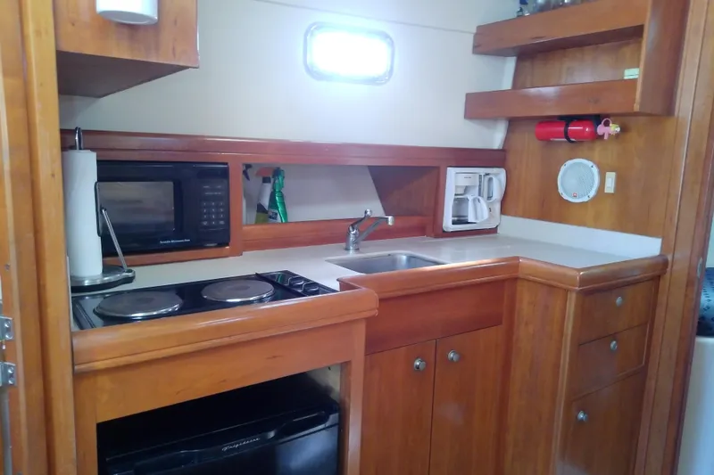 Slide: The Image of 2004 Mainship 34 Pilot II galley with stove, microwave, sink, and wooden cabinetry. - 45