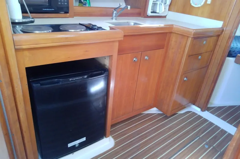 Slide: The Image of 2004 Mainship 34 Pilot II galley with wood cabinetry, compact fridge, and stove. - 46