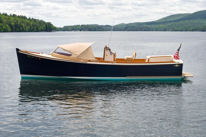Slide: The Image of 2016 First Light Monomoy 26 boat on a serene lake with lush green hills. - 3