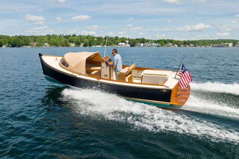 Slide: The Image of 2016 First Light Monomoy 26 boat cruising on a lake with American flag. - 0
