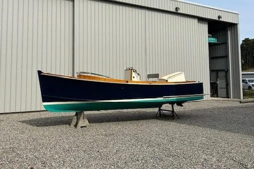 Slide: The Image of 2016 First Light Monomoy 26 boat on stands outside a metal building. - 4