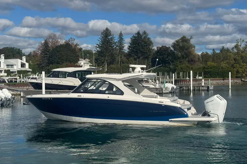 Slide: The Image of 2025 Regal LX36 boat docked in a scenic marina with clear skies. - 2