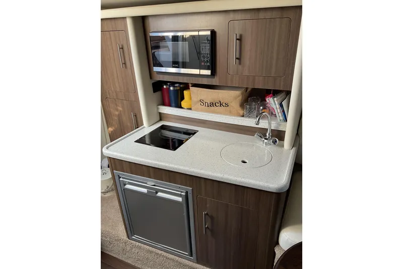 Slide: The Image of 2019 Rinker 290 Express Cruiser kitchenette with microwave, sink, and storage cabinets. - 15