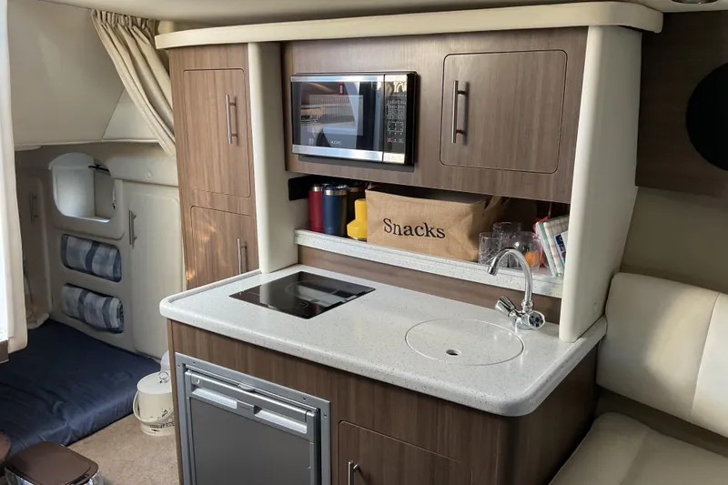 Slide: The Image of 2019 Rinker 290 Express Cruiser interior kitchen with microwave, sink, and storage. - 16