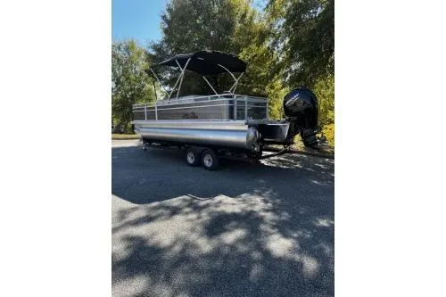 Slide: The Image of 2026 Sun Tracker Fishin' Barge 22 DLX pontoon boat on trailer, parked outdoors. - 2