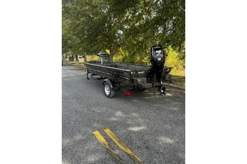 Slide: The Image of 2026 Tracker Grizzly 1654 T Sportsman boat on trailer, parked on a tree-lined road. - 2