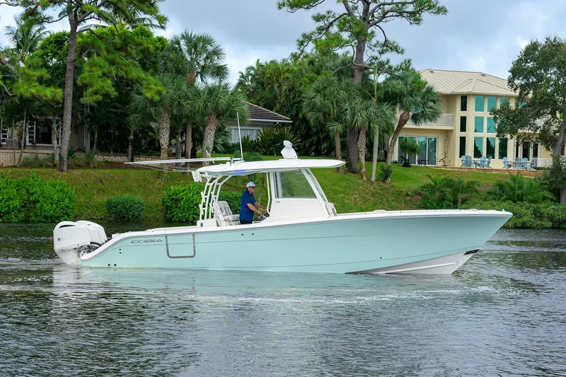 The Image of 2020 Cobia 350 CC boat cruising on a scenic waterway near lush greenery. - 0